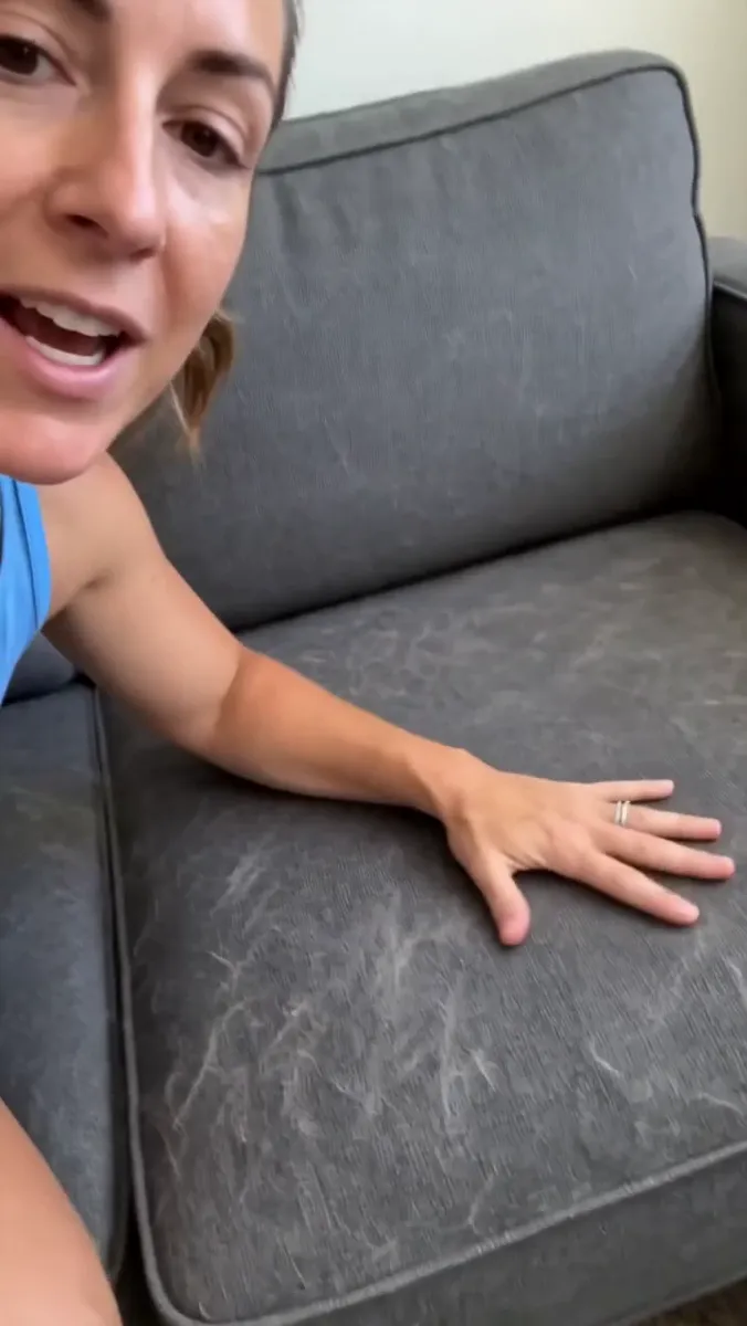 Close selfie of a woman pressing her palm on a grey sofa cushion covered in pet hair