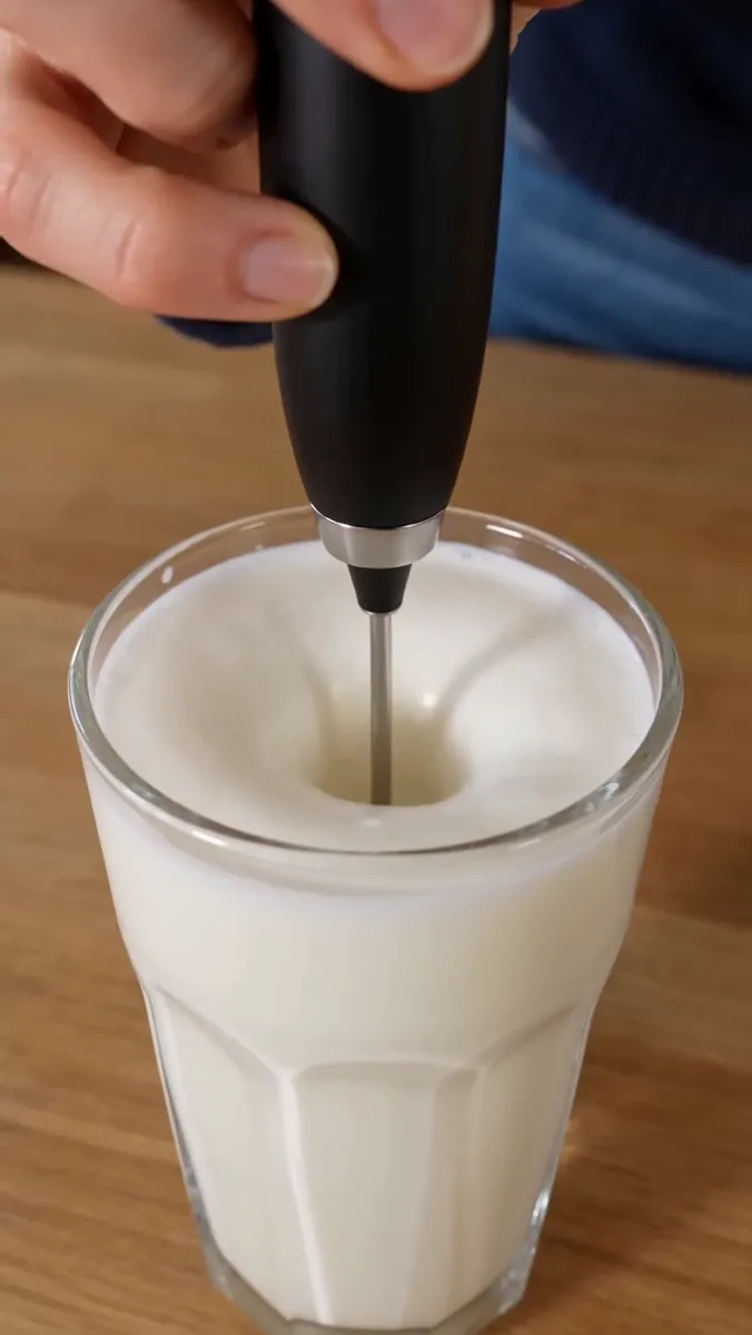 Close-up of the milk in the glass, now thick with foam around the frother stem